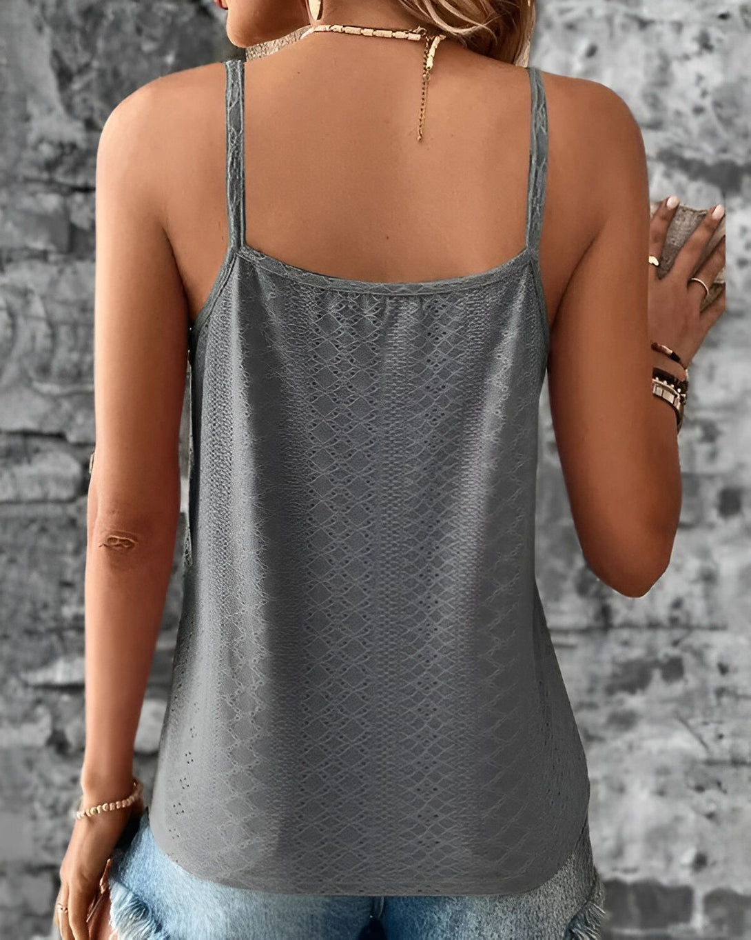 Une femme porte un débardeur gris à fines bretelles. Le débardeur est en dentelle et présente un motif géométrique. La femme est vue de dos.