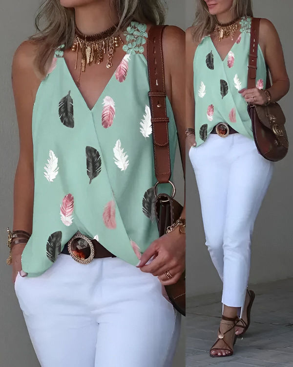 Une femme porte un haut vert à motifs de plumes avec un pantalon blanc et des sandales marron. Elle a un collier et un sac à main marron.