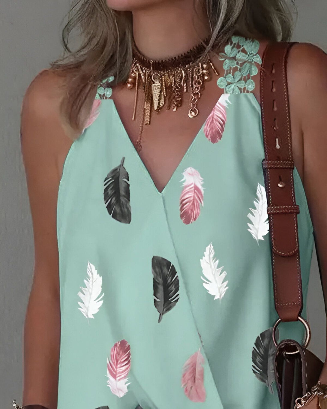 Une femme porte un chemisier vert à motifs de plumes avec un jean et un collier doré.