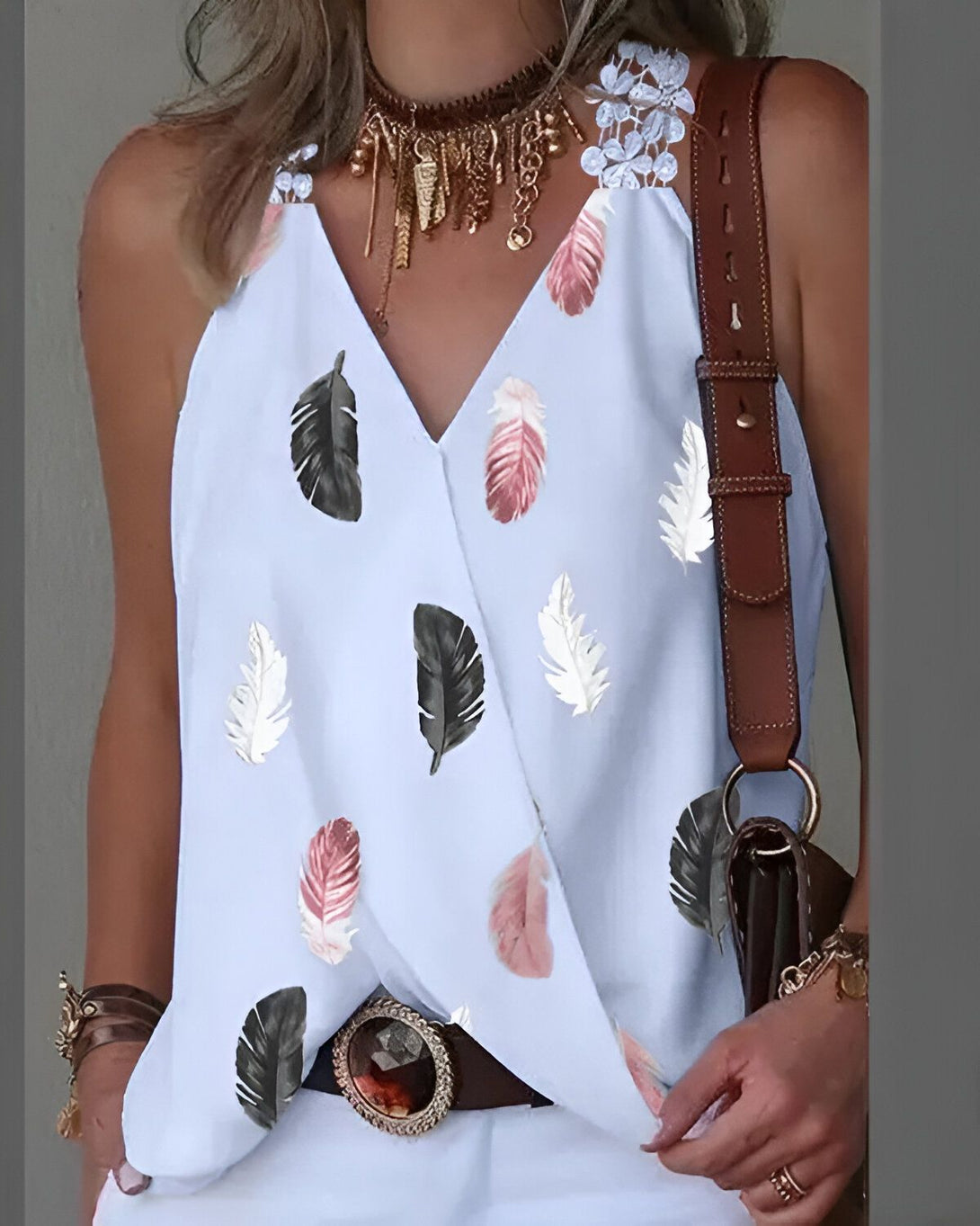 Une femme porte un débardeur blanc à motifs de plumes colorées. Elle porte également un collier et une ceinture marron.