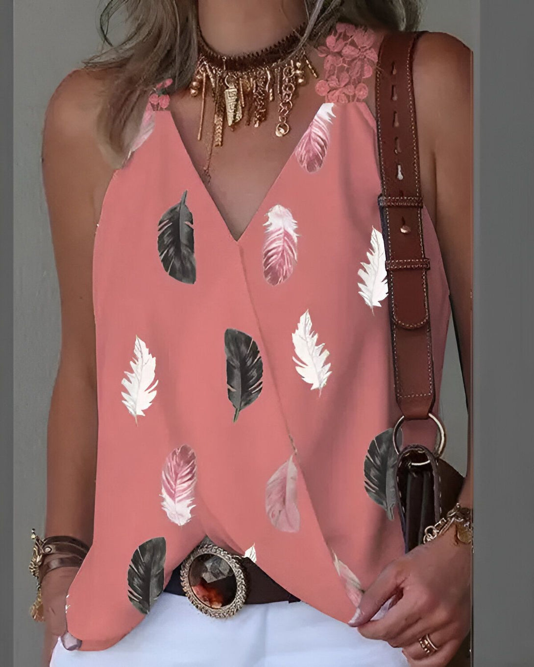 Une femme porte un débardeur rose à motifs de plumes. Le débardeur est décolleté en V et possède des bretelles fines. La femme porte également un pantalon blanc et une ceinture marron.