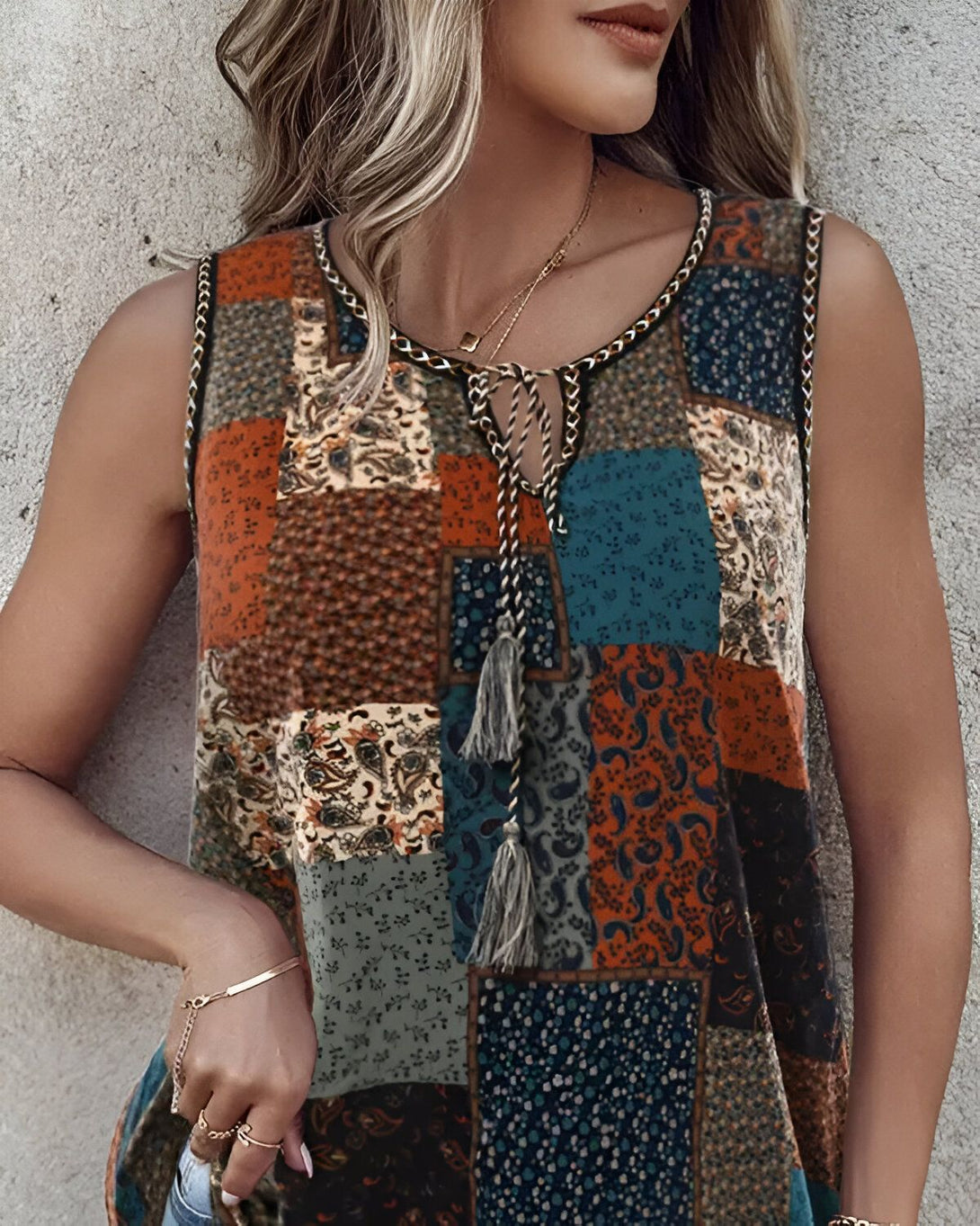 Une femme porte un débardeur marron et bleu à motifs cachemire et paisley. Le débardeur est noué au niveau du cou et possède des détails en dentelle.