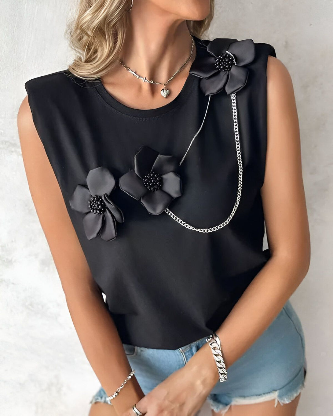 Une femme porte un t-shirt noir sans manches avec des fleurs en tissu noir et des chaînes.