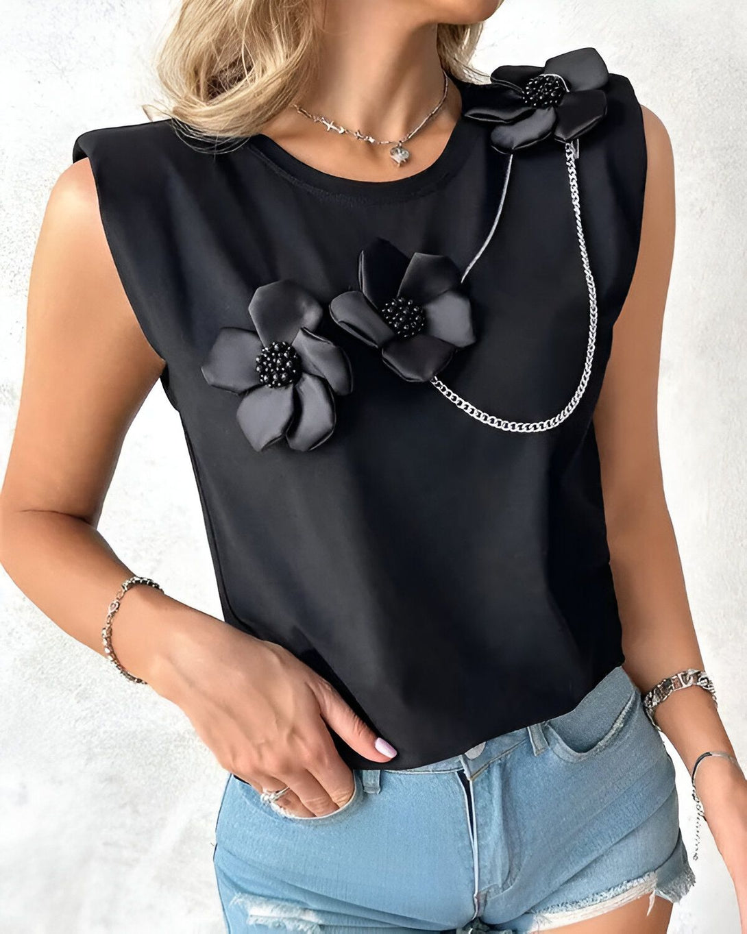 Une femme porte un t-shirt noir sans manches avec des fleurs en tissu noir et des chaînes.