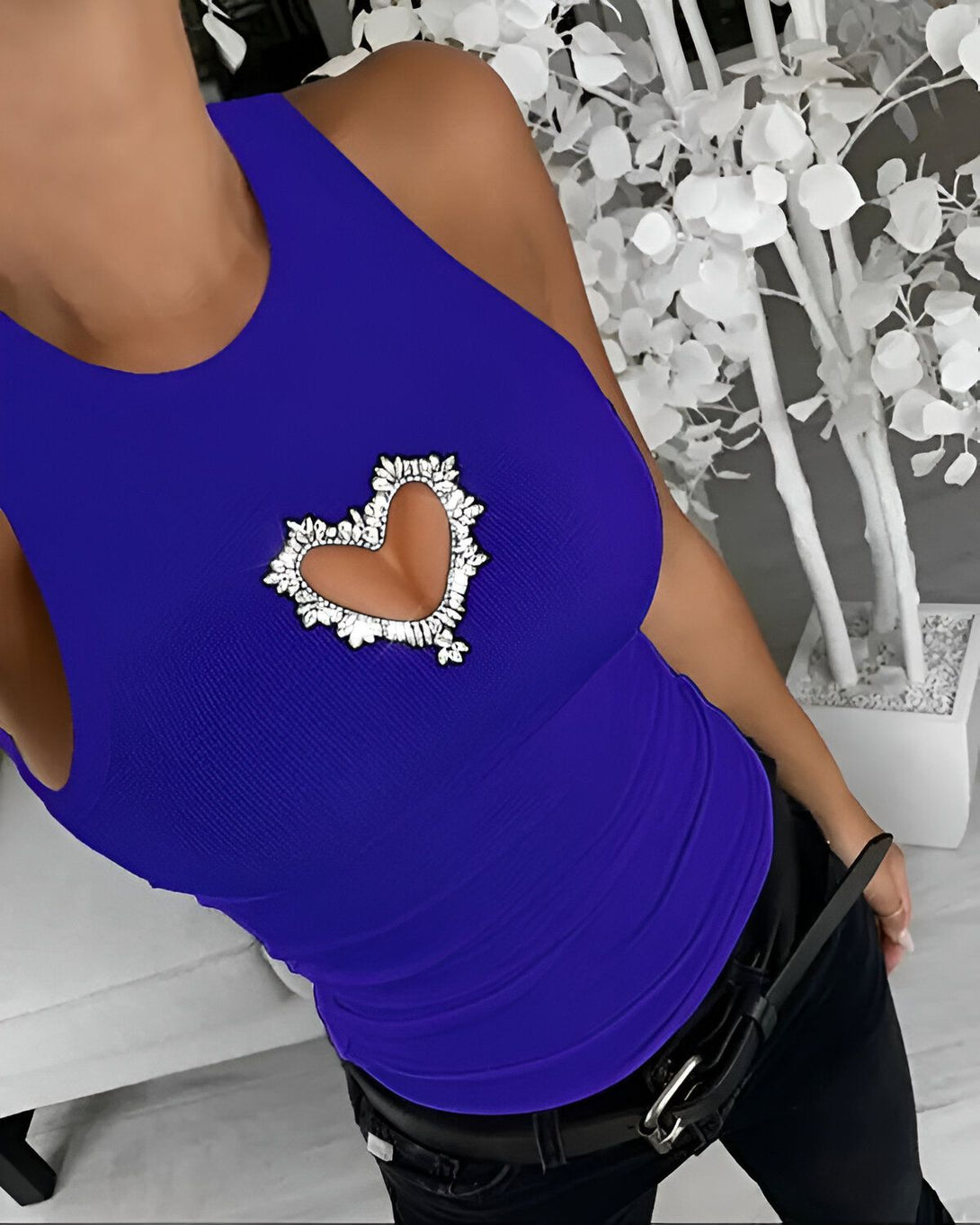 Une femme porte un débardeur bleu avec un cœur en strass sur la poitrine.