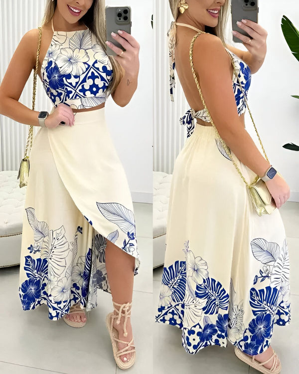 Une femme porte un ensemble deux pièces composé d'un crop top et d'une jupe longue. Le crop top est bleu et blanc, avec un motif floral. La jupe est blanche, avec un motif de feuilles tropicales bleues. La femme est également porte des sandales beiges et un sac à main doré.