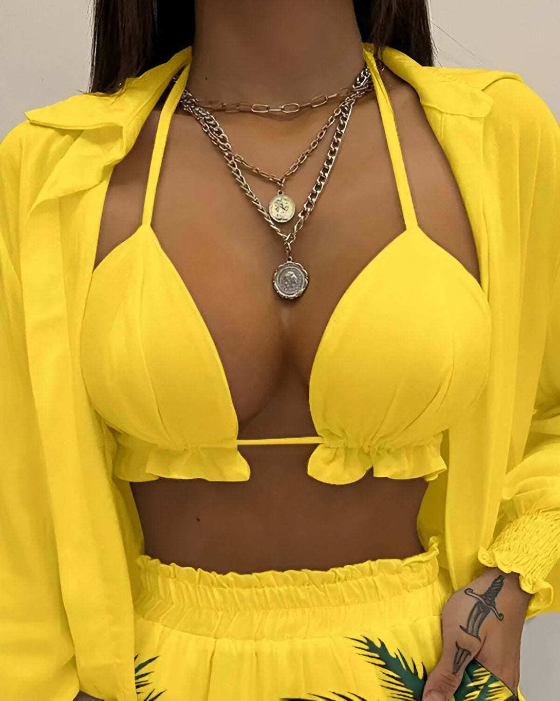 Une femme porte un haut de bikini jaune et un pantalon assorti. Elle porte également plusieurs colliers et un bracelet.