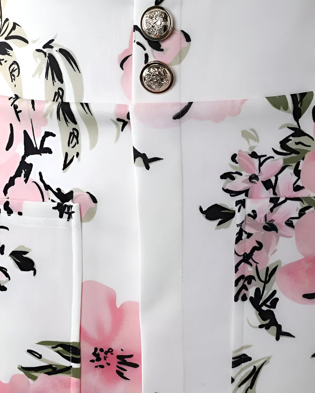 Une image d'un pantalon blanc à motifs floraux roses et noirs. Le pantalon est fermé par deux boutons dorés.
