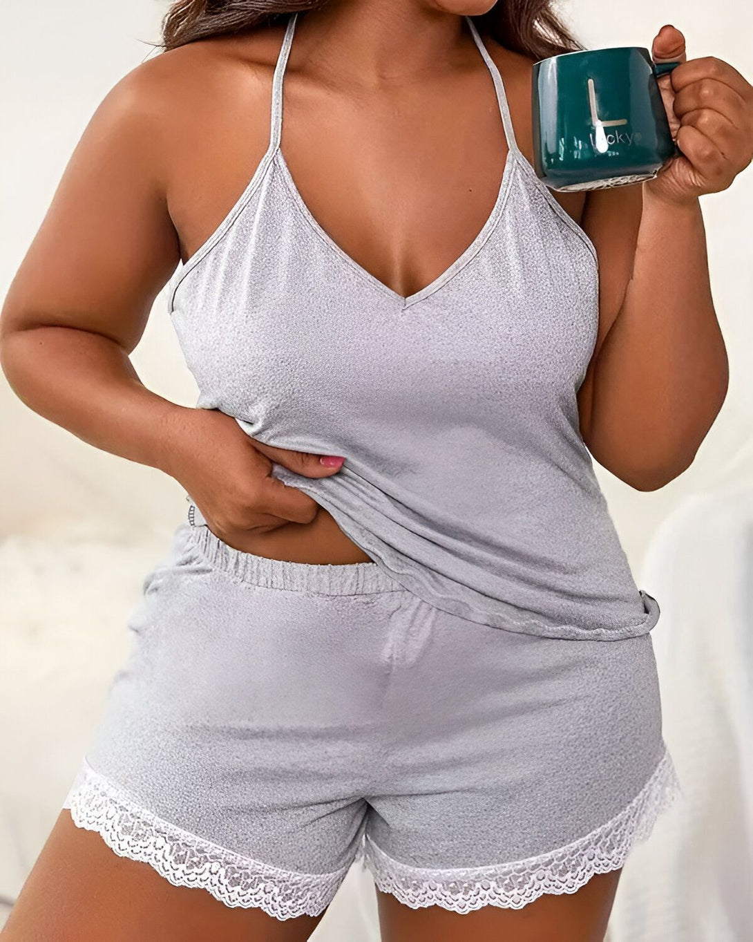 Une femme porte un ensemble de pyjama gris. Le haut est une camisole à bretelles avec un décolleté en V. Le short est court et possède une taille élastique. L'ensemble est en dentelle.