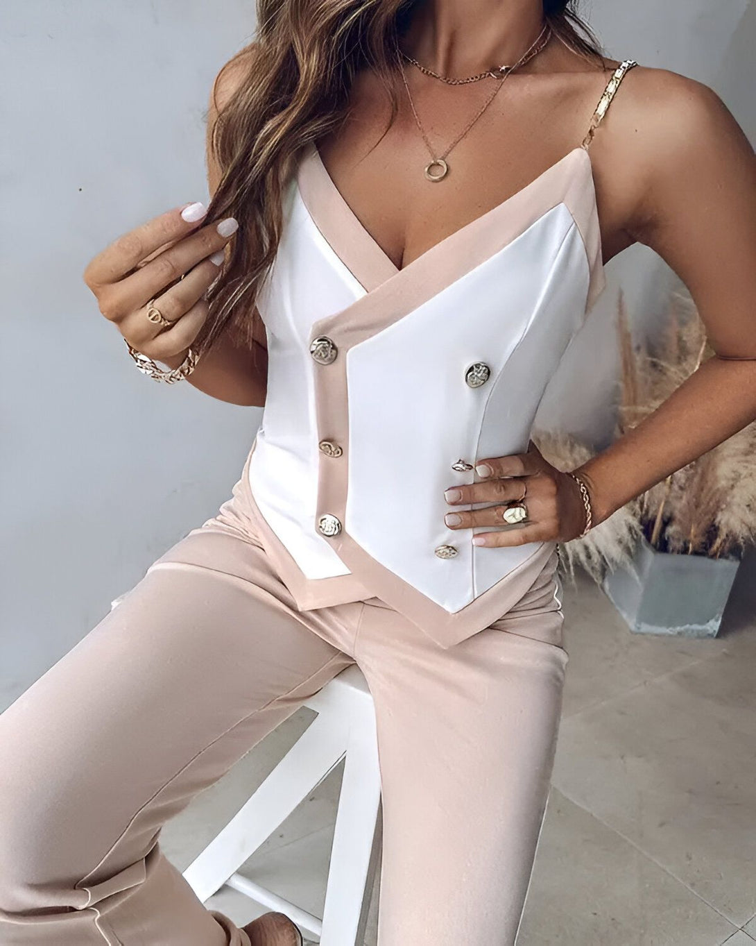 Une femme porte un pantalon beige et un haut beige et blanc. Le haut est décolleté et possède des boutons dorés.