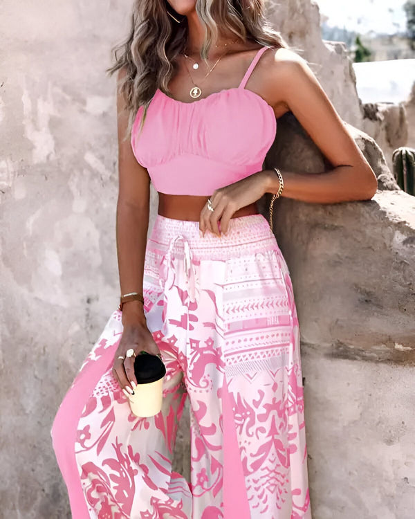 Une femme porte un haut court rose et un pantalon large rose et blanc. Elle tient une tasse à café à la main.