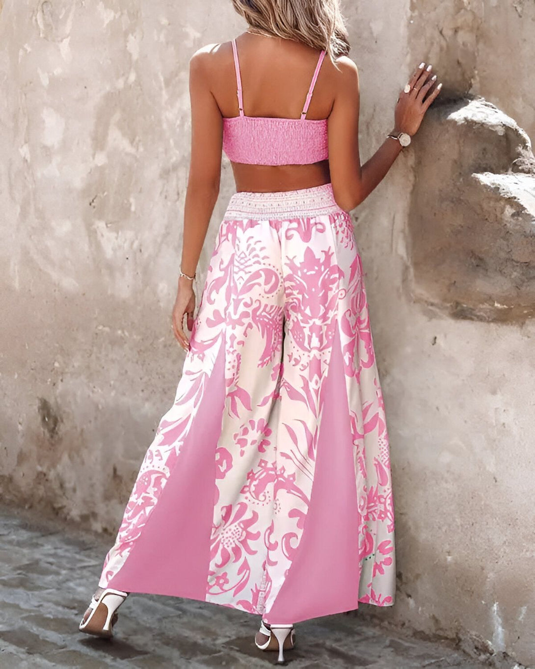 Une femme porte un haut court rose et un pantalon large rose à motifs. Le pantalon est fendu sur les côtés.