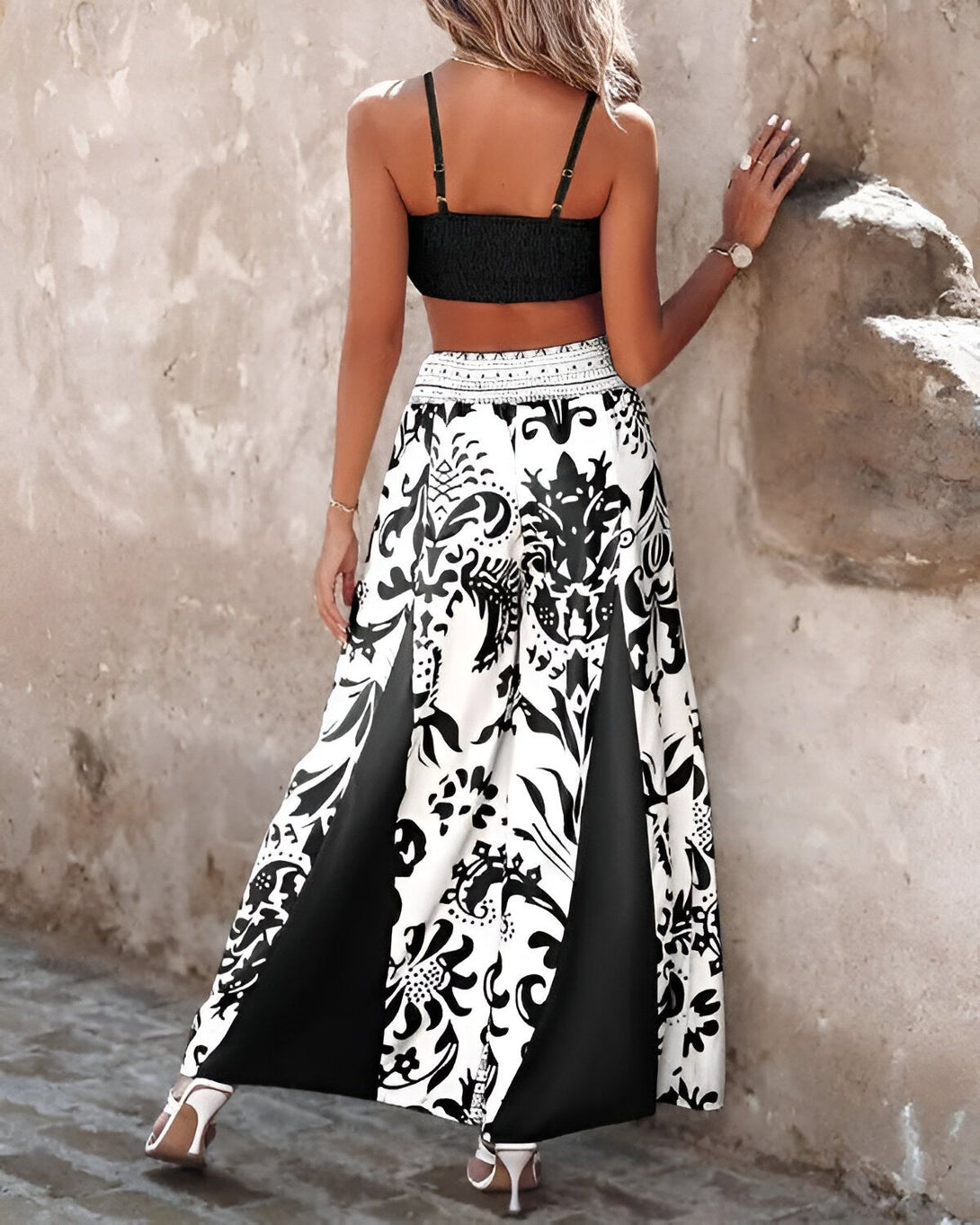 Une femme porte un pantalon large noir et blanc à motifs et un haut court noir. Elle est vue de dos.