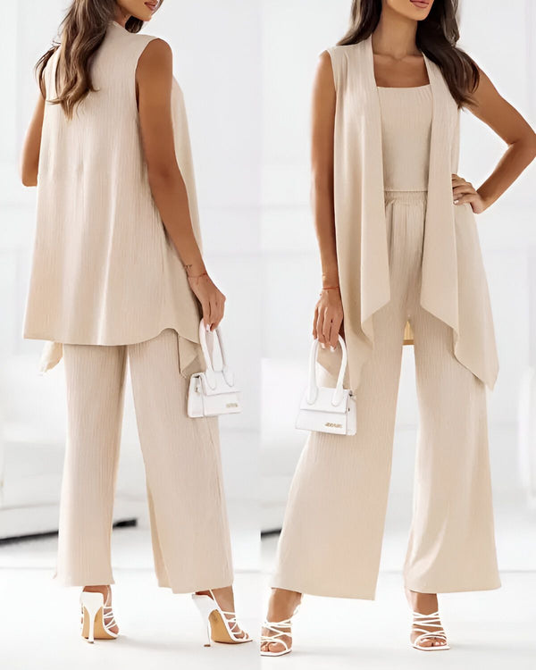 Une femme porte un gilet beige, un pantalon beige et des sandales beiges. Elle porte également un sac à main blanc.
