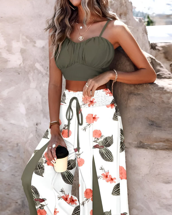 Une femme porte un haut court vert olive et un pantalon taille haute à imprimé floral. Elle est debout près d'un mur et tient une tasse à la main.