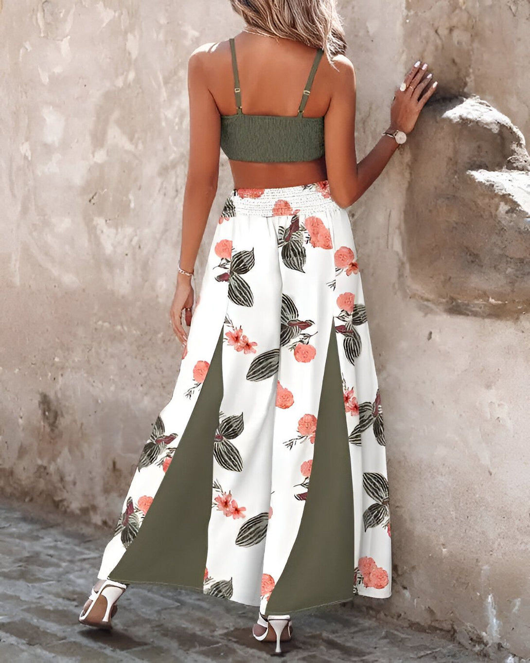 Une femme porte un haut court vert et un pantalon long fleuri blanc et vert. Le pantalon est fendu sur les côtés.