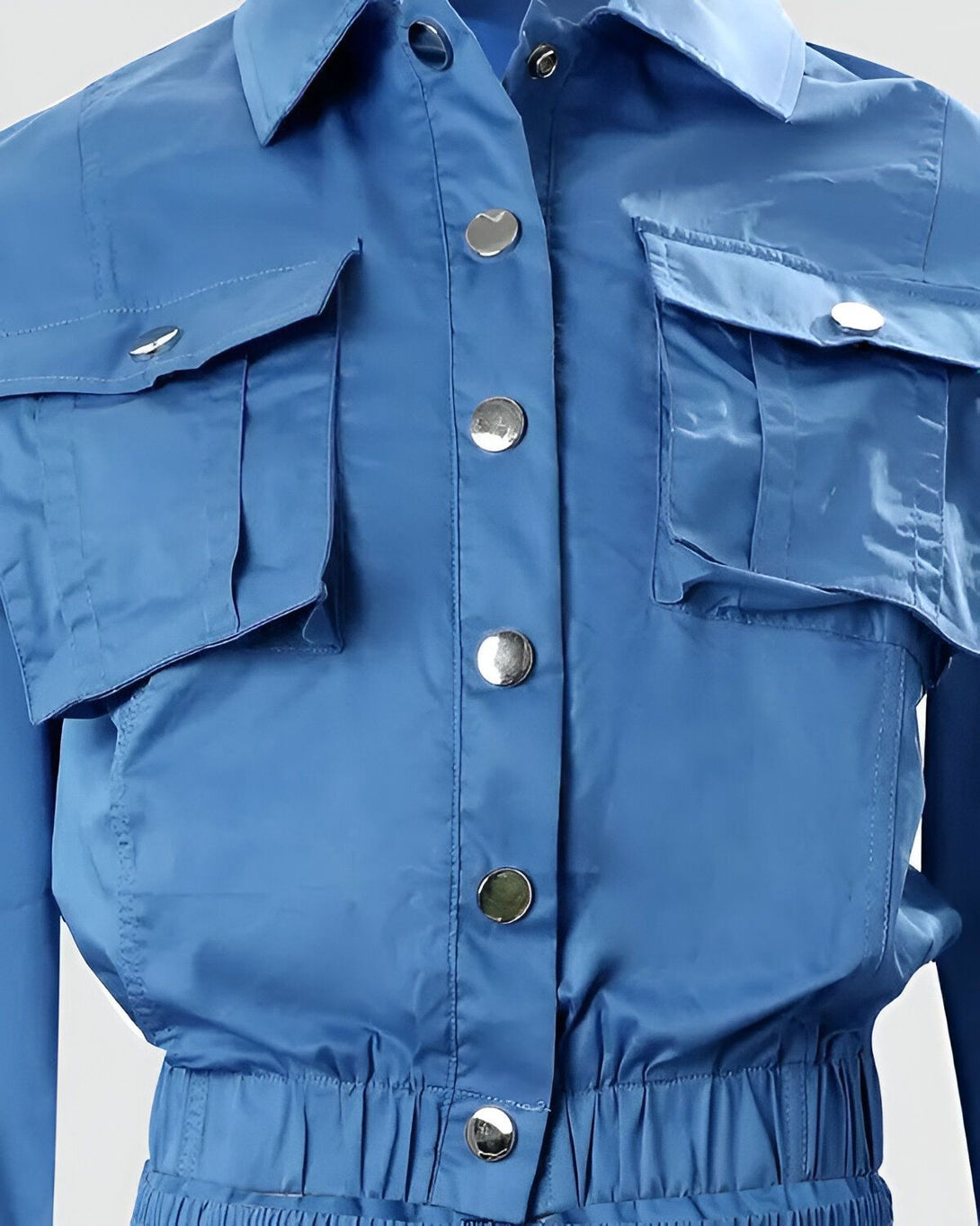 Une image d'une combinaison bleue avec des boutons argentés. La combinaison est cintrée à la taille et possède des poches à rabat sur la poitrine.