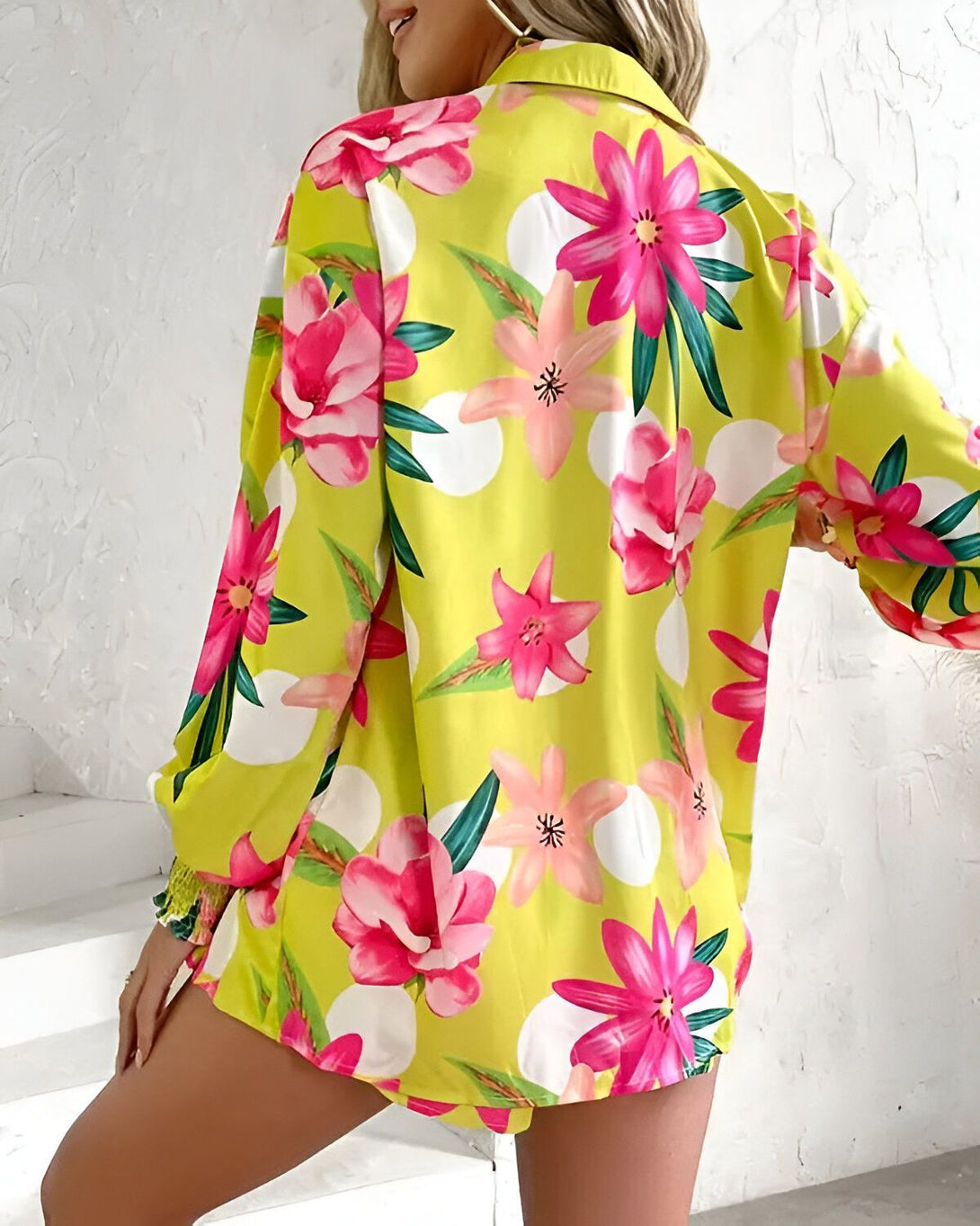Une femme porte une chemise jaune à fleurs roses et blanches. La chemise est ouverte et on peut voir son dos. Elle porte également un short jaune.