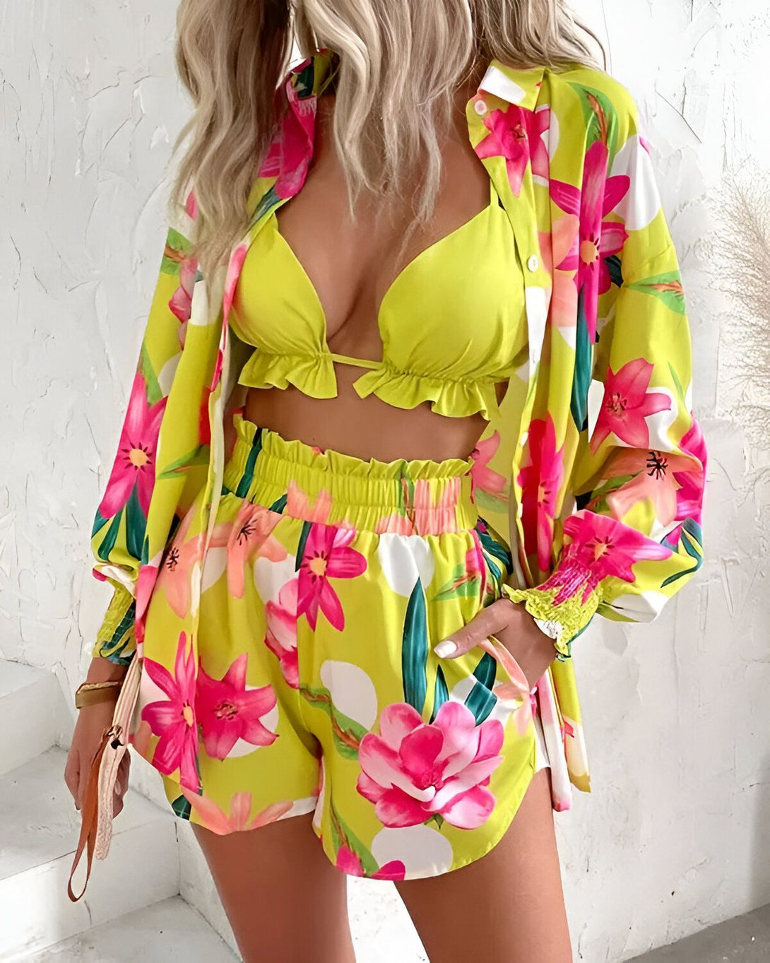 Une femme porte un ensemble trois pièces jaune et rose à motifs floraux. Il est composé d'un short, d'une chemise et d'un soutien-gorge.