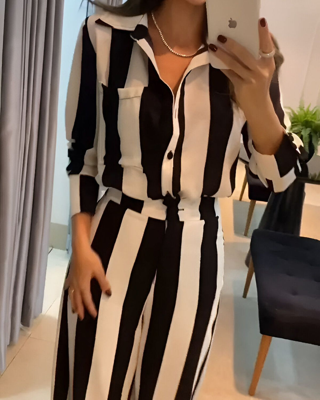 Une femme porte un chemisier et un pantalon rayés noirs et blancs. Elle a un collier et une bague.