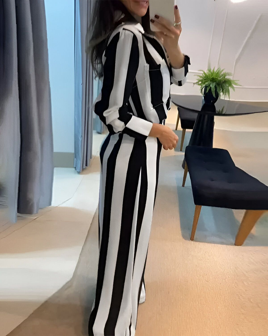 Une femme porte un pantalon et une veste à rayures noires et blanches. Elle est vue de dos et se tient debout dans une pièce.