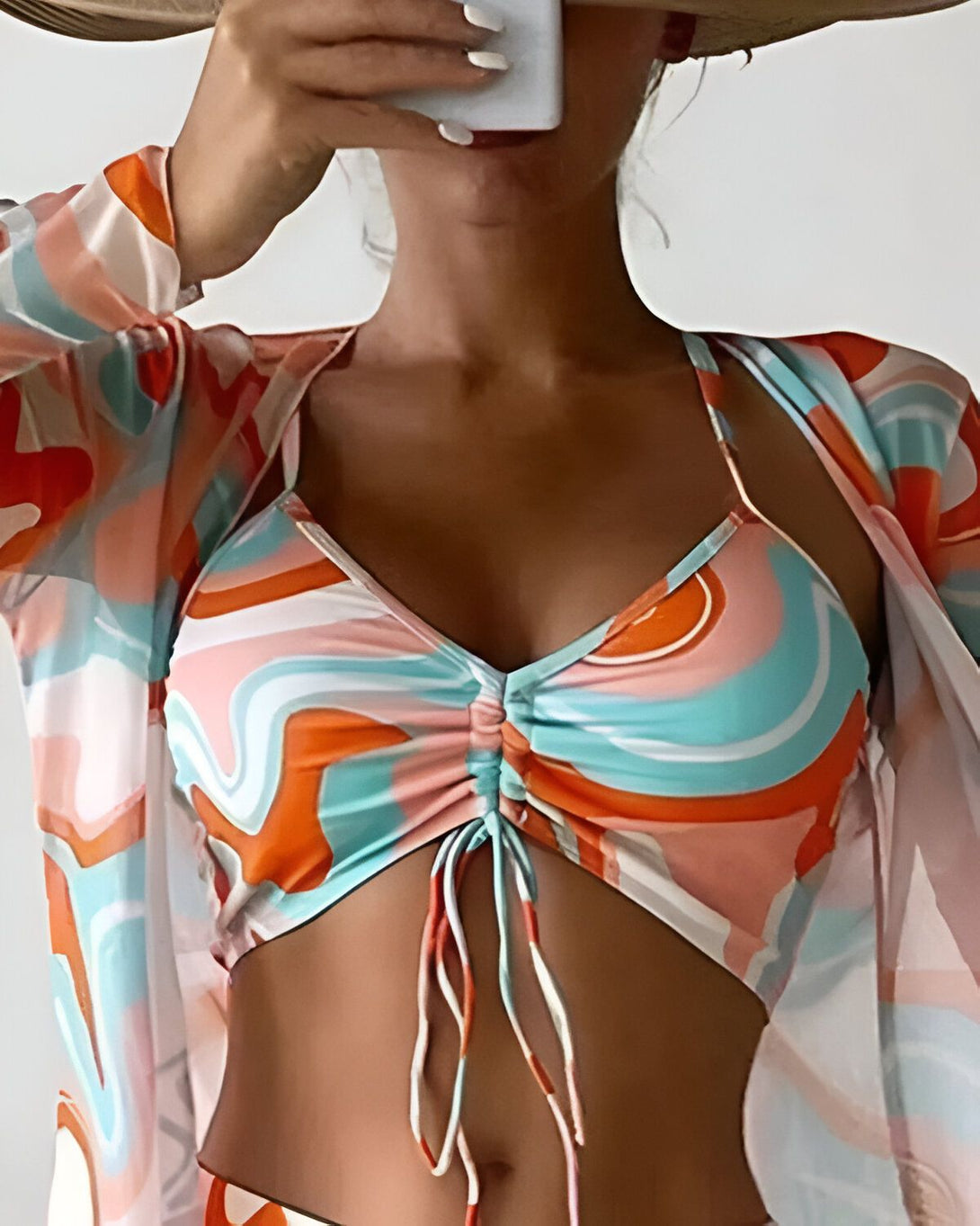 Une femme porte un bikini orange et bleu à motifs et une chemise blanche transparente.