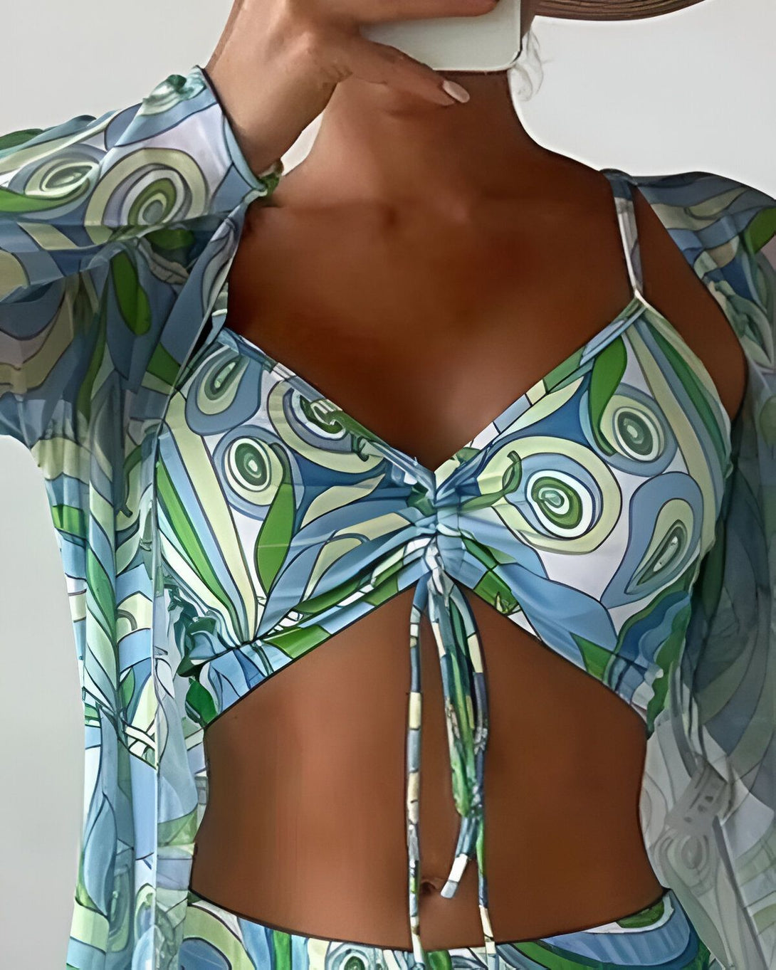 Une femme porte un haut de bikini bleu et vert à motifs psychédéliques et un pantalon assorti. Elle porte également une longue robe de plage transparente.