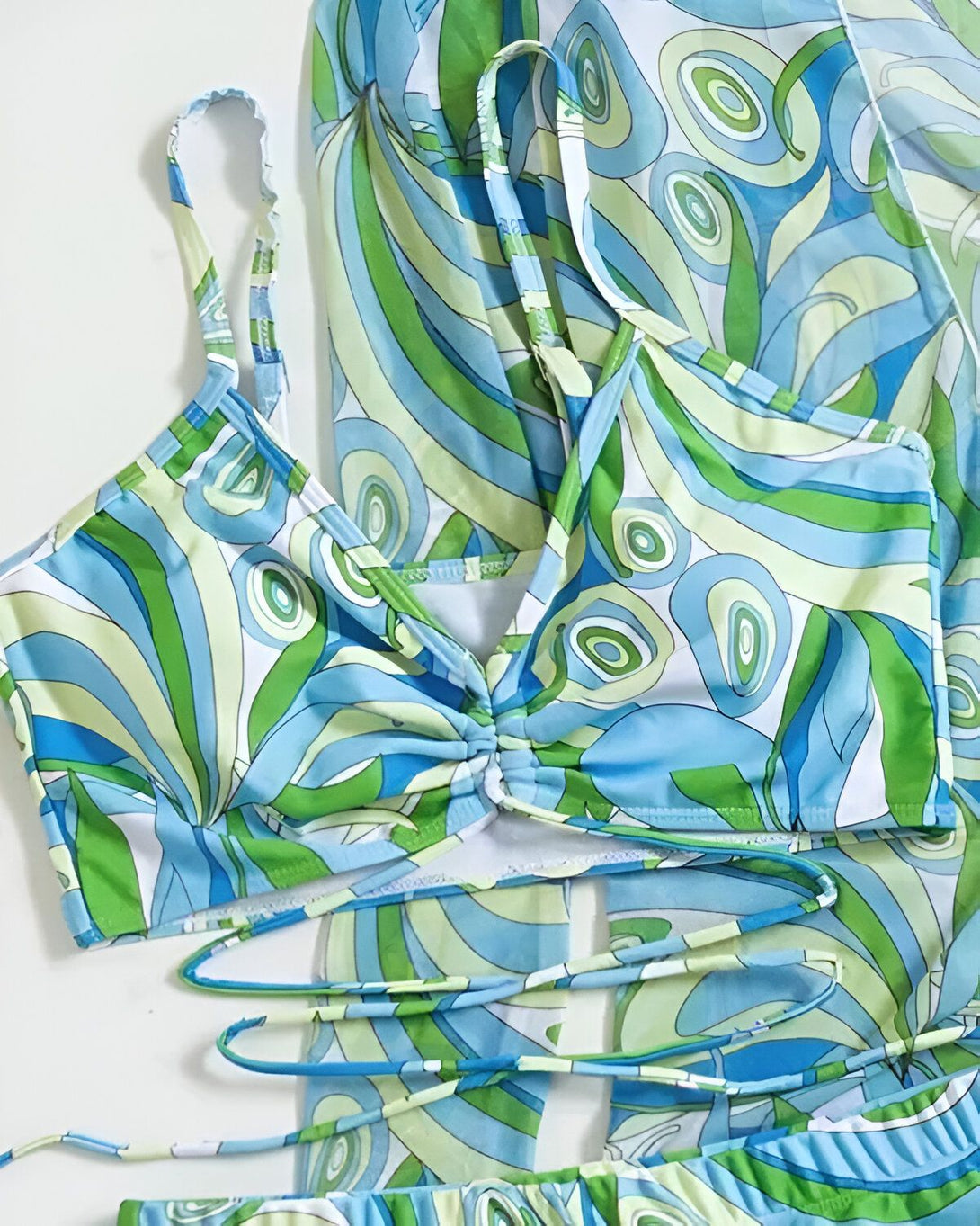 Un maillot de bain deux pièces bleu et vert à motifs psychédéliques, avec un haut de bikini triangle à armatures et des liens à nouer autour du cou et du dos, et un bas de bikini échancré à taille haute.