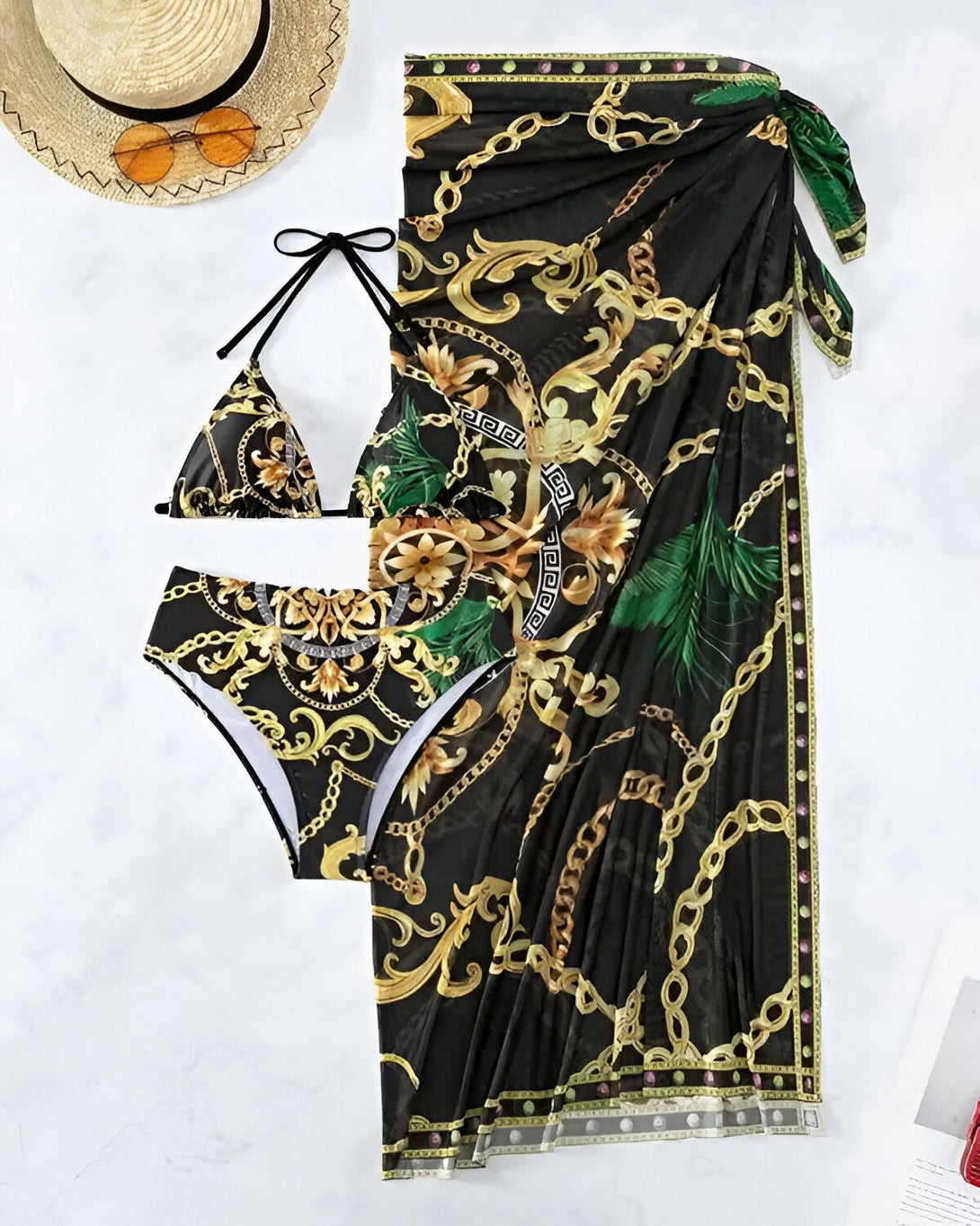 L'image représente un maillot de bain deux pièces avec un paréo assorti. Le maillot de bain est de couleur noire et or avec un motif de chaînes et de feuilles tropicales. Le paréo est de la même couleur et du même motif que le maillot de bain. Il est noué autour de la taille et peut être porté de différentes manières.