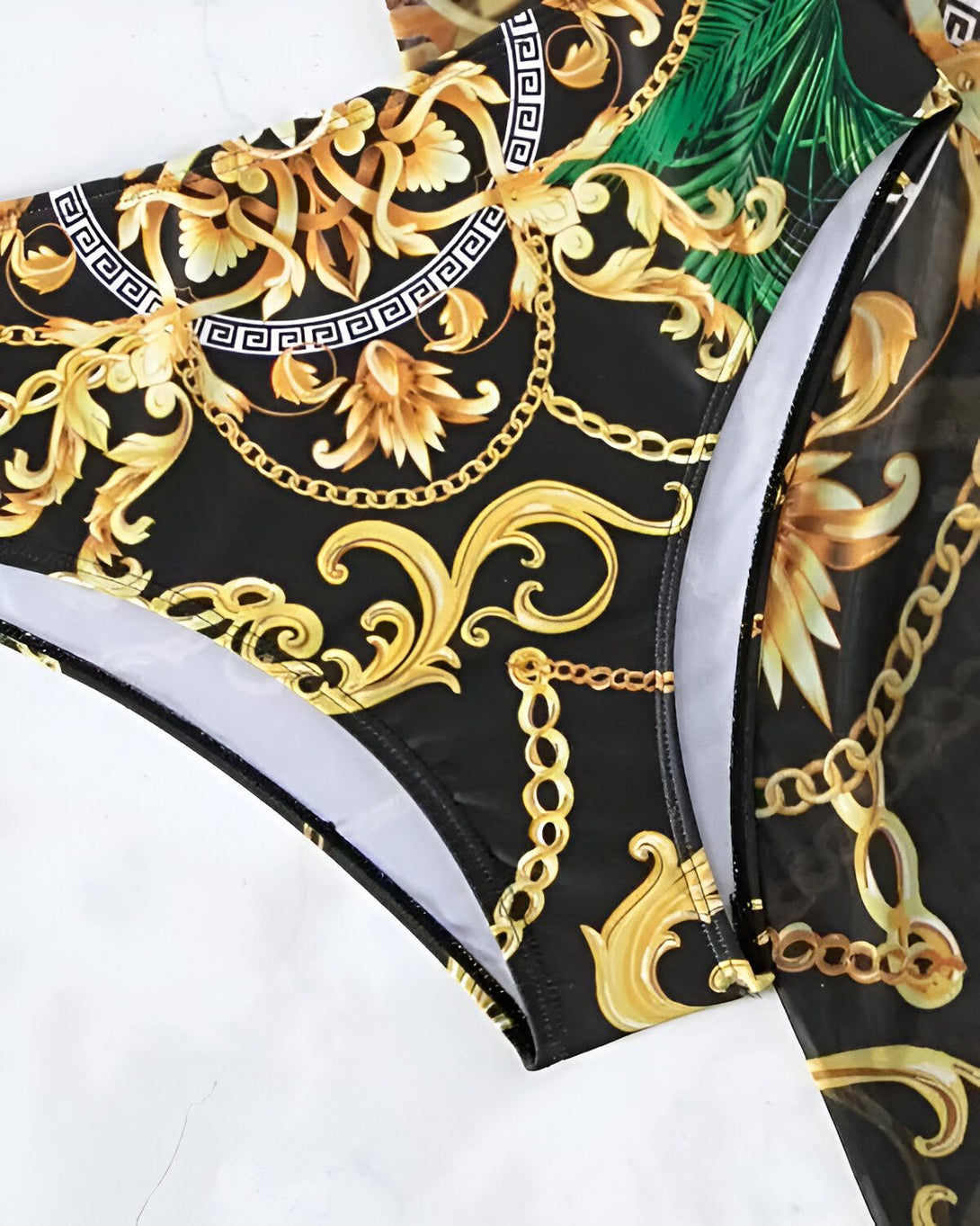 L'image montre un maillot de bain deux pièces avec un haut de bikini et un bas de bikini. Le haut de bikini est noir avec un motif de chaînes dorées et de feuilles tropicales vertes. Le bas de bikini est noir avec le même motif que le haut.