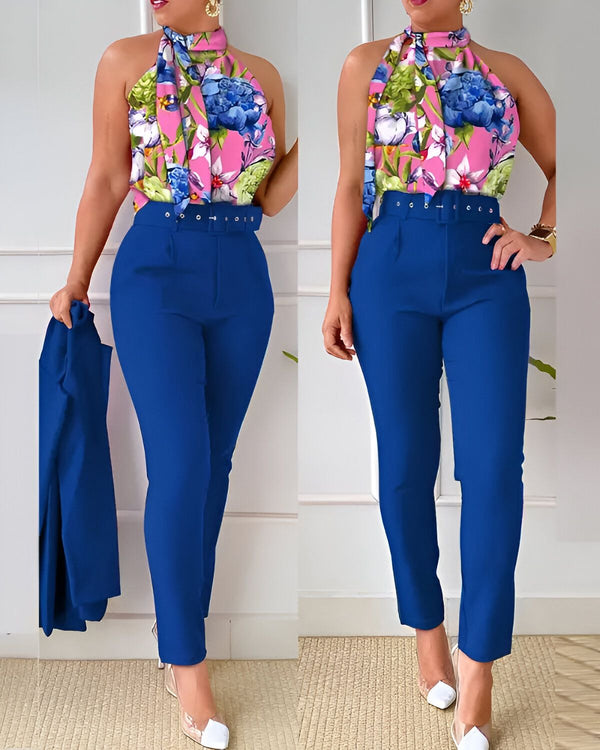 Une femme porte un pantalon bleu marine taille haute et un chemisier à fleurs rose et bleu avec un blazer bleu marine à la main.
