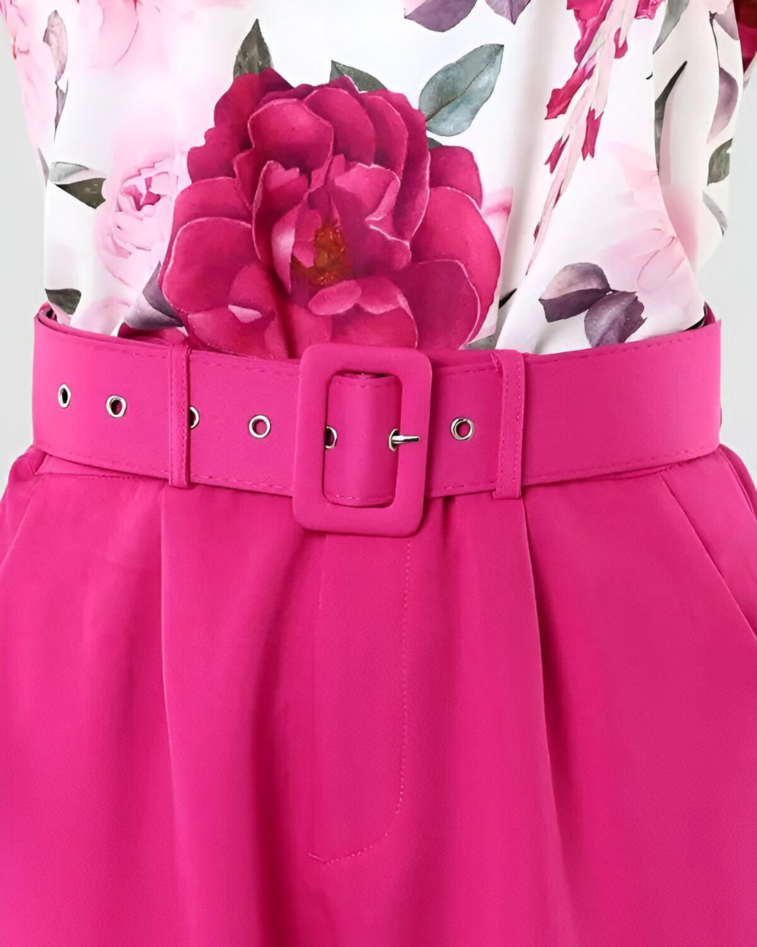 Une image d'une ceinture rose avec une boucle carrée sur un pantalon rose. Le pantalon est porté avec une chemise blanche à fleurs roses.