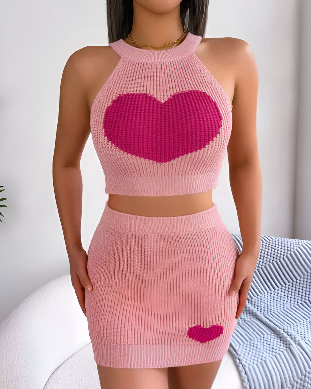 Une femme porte un ensemble deux pièces rose avec un motif de cœur. Le haut est un crop top avec un col montant et le bas est une jupe courte.