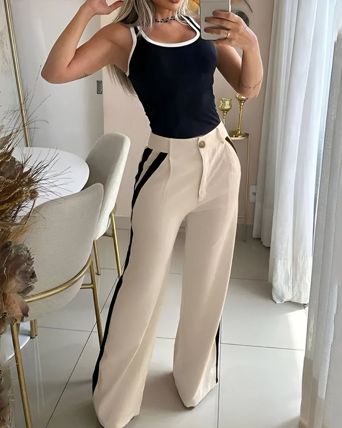 Une femme porte un débardeur noir et un pantalon beige taille haute avec des rayures noires sur les côtés.