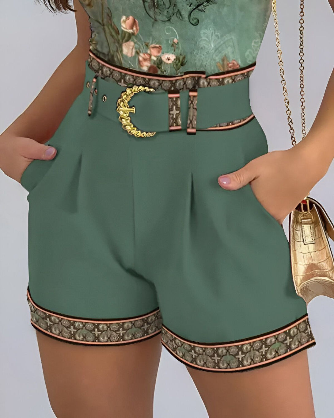 Une femme porte un short vert taille haute avec une ceinture dorée. Le short est orné d'un motif floral sur les côtés.
