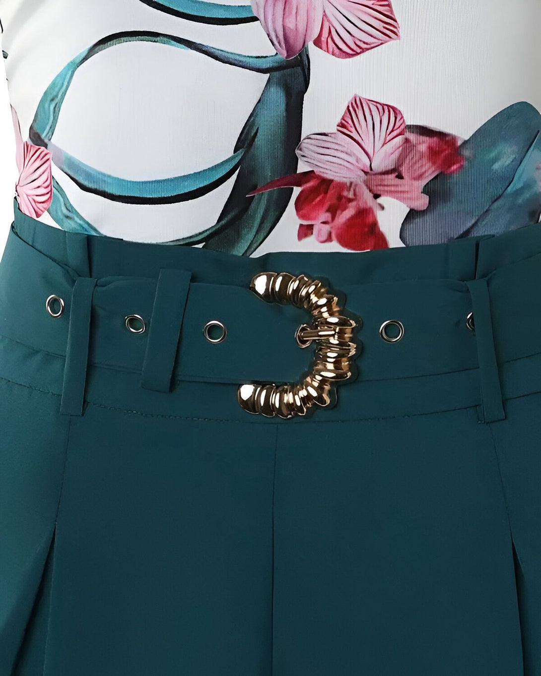 Une image d'un pantalon taille haute vert foncé avec une ceinture dorée. Le pantalon est porté avec un chemisier blanc à fleurs roses et vertes.
