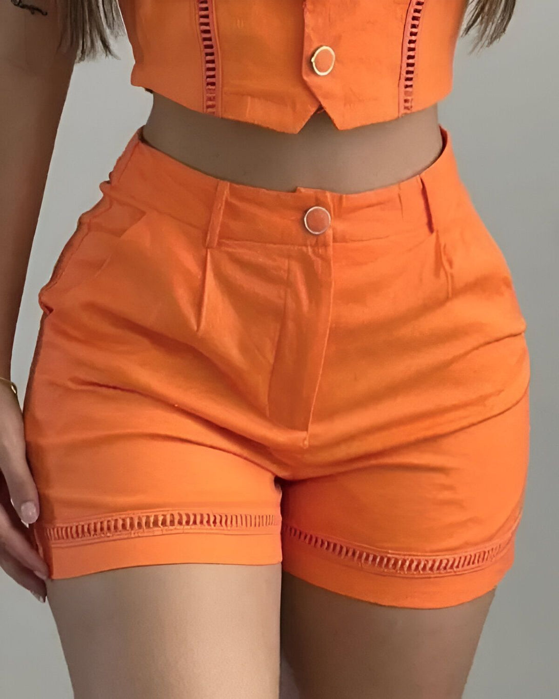 Une femme porte un short orange taille haute. Le short est froncé sur les côtés et possède des poches.