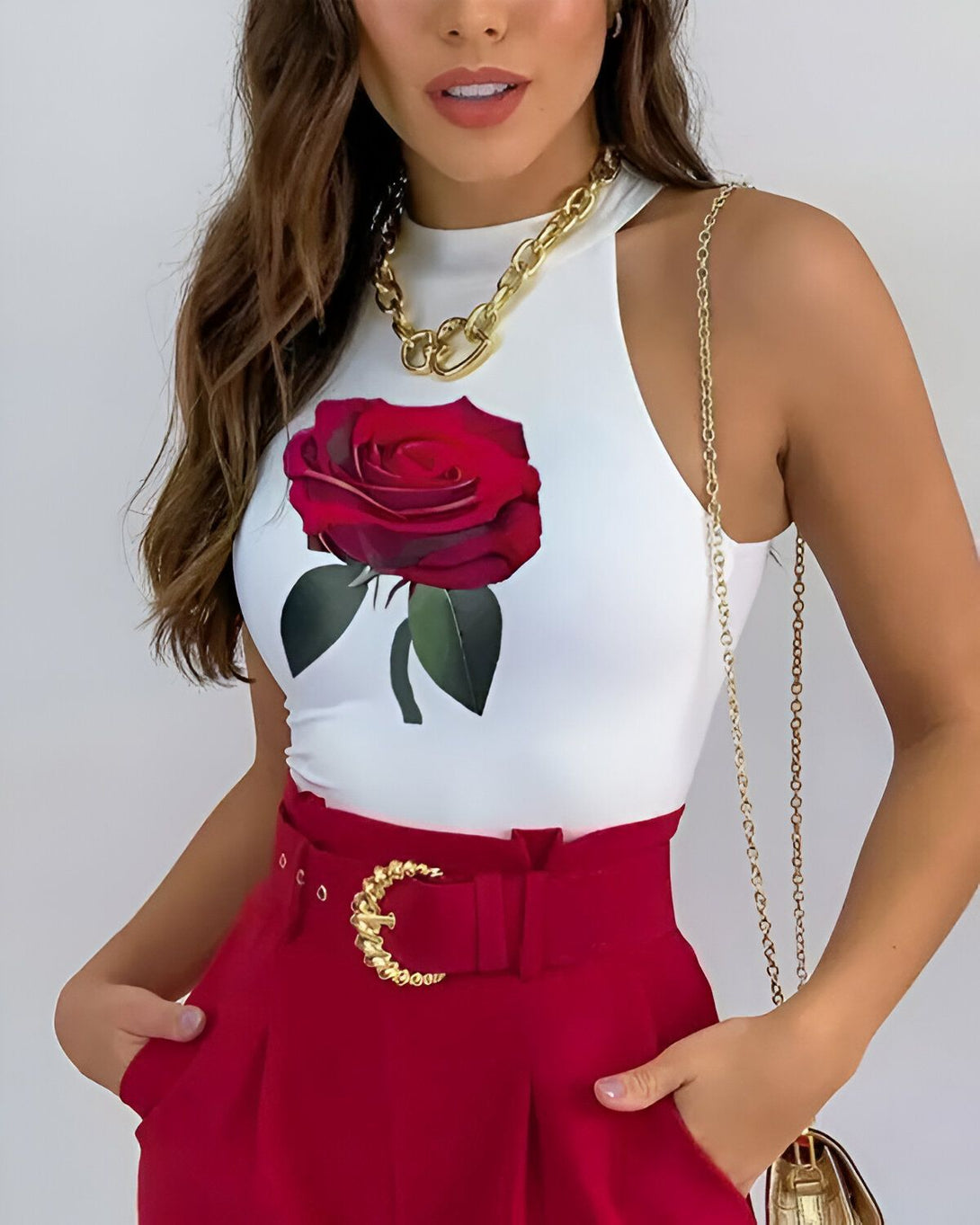 Une jeune femme porte un haut blanc avec une image de rose rouge, un pantalon rouge et un collier doré.