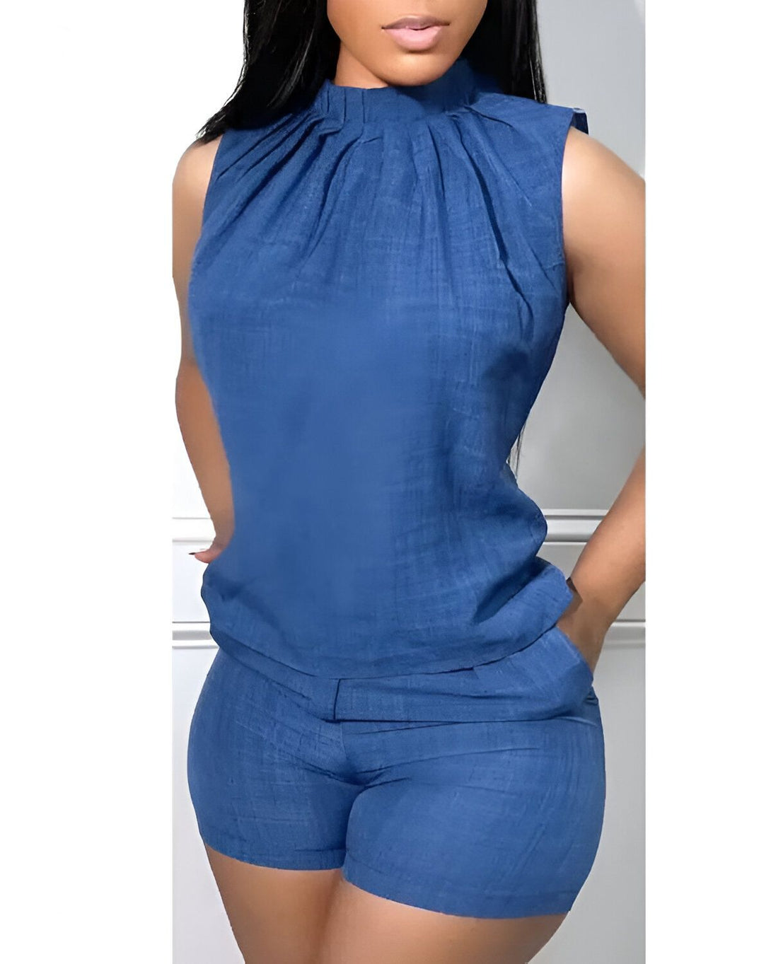 Une femme porte un ensemble de couleur bleu composé d'un top et d'un short. Le top est sans manches et possède un col montant. Le short est taille haute et possède des poches latérales.