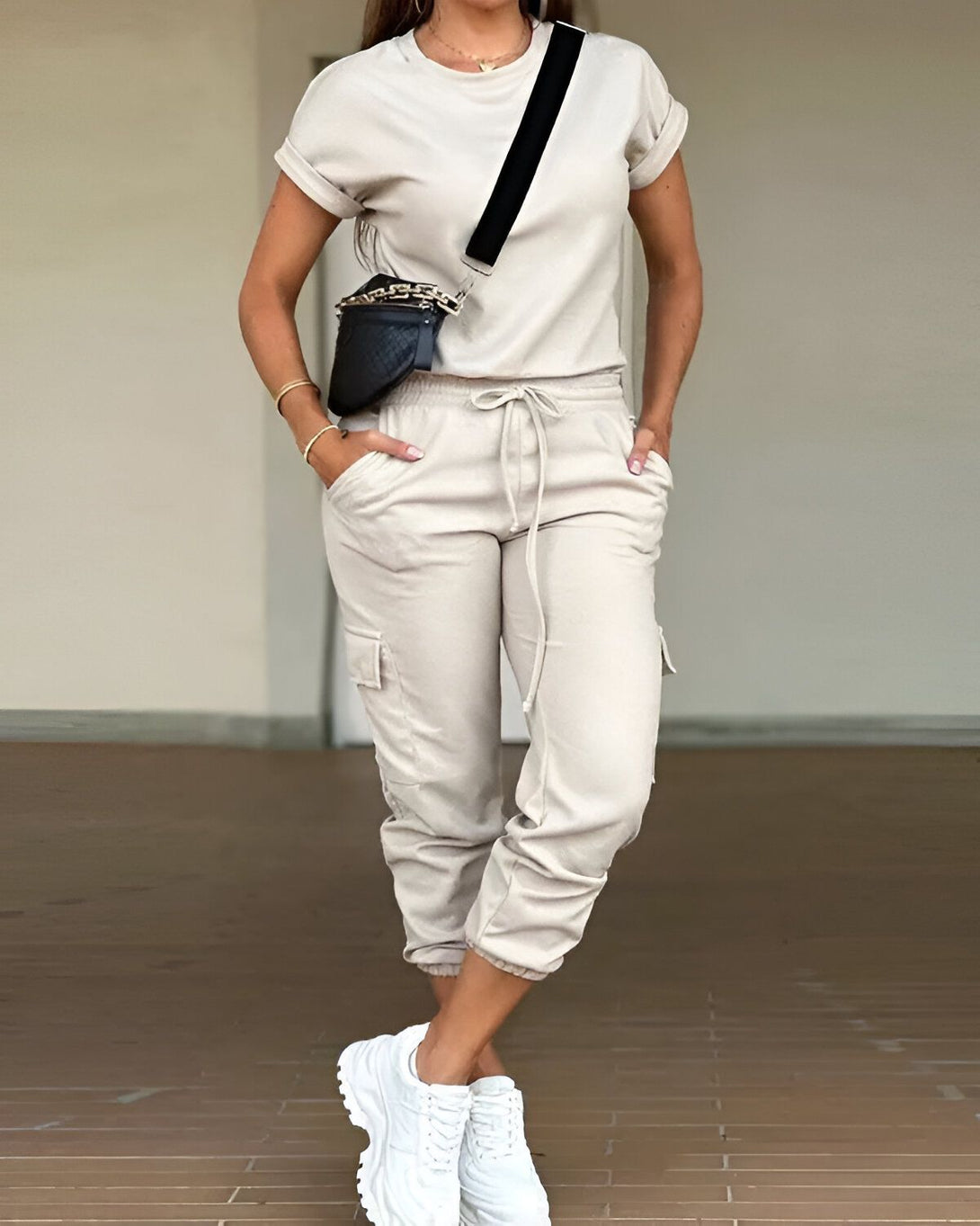 Une femme porte un t-shirt beige et un pantalon cargo beige. Elle a un sac à main noir et des baskets blanches.