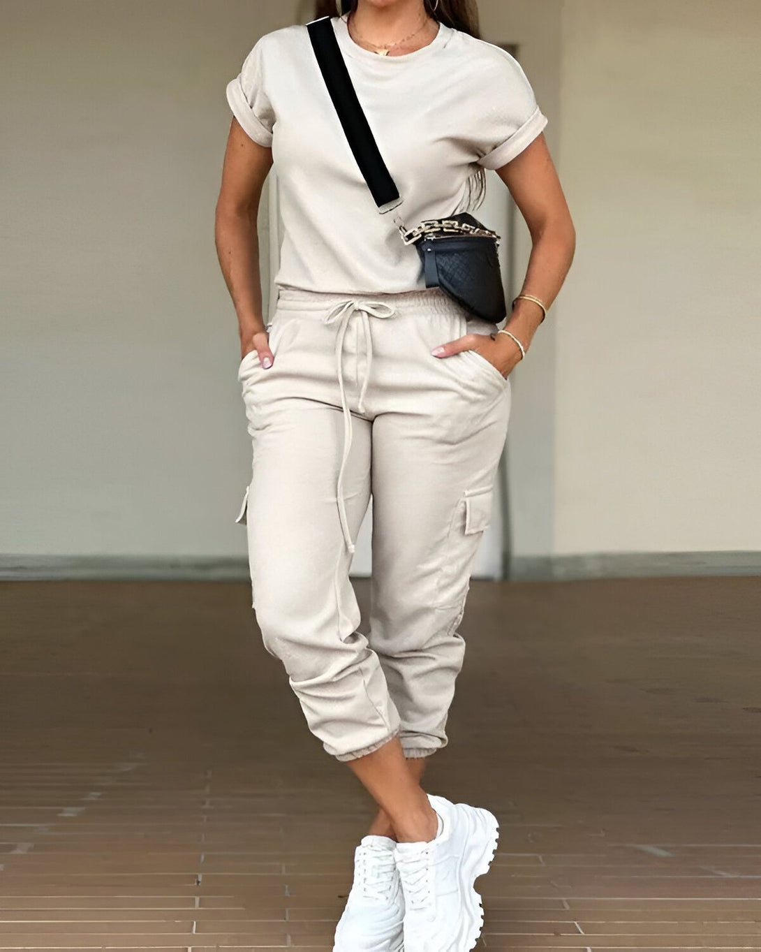 Une femme porte un ensemble beige composé d'un t-shirt à manches courtes et d'un pantalon cargo. Elle porte également des baskets blanches et un sac à main noir.