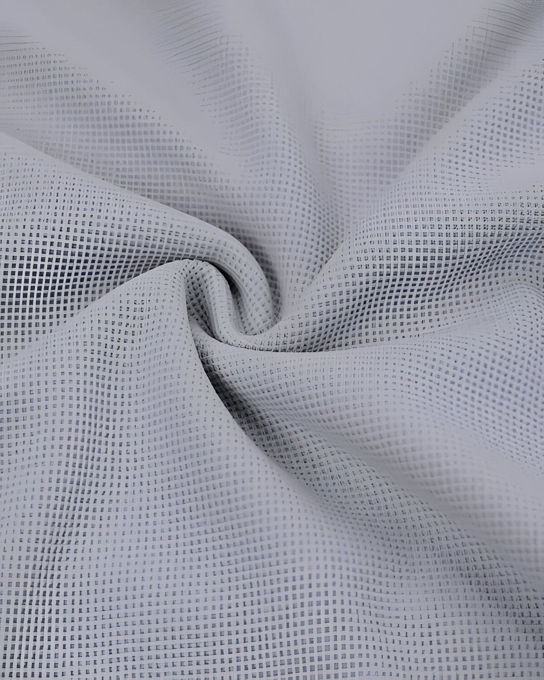 L'image montre un tissu blanc avec un motif de petits carrés. Le tissu est froissé et on peut voir les plis.