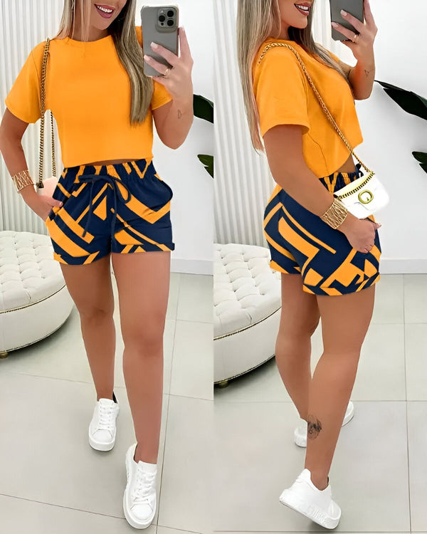Une femme porte un ensemble short et haut jaune et bleu. Le haut est court et moulant, et le short est ample et a une taille haute. La femme est debout et prend une photo d'elle-même dans un miroir.