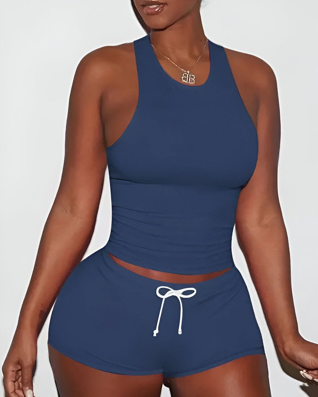 Une femme porte un débardeur et un short bleu marine. Le débardeur est court et moulant, et le short est taille haute et possède un cordon de serrage à la taille. La femme est debout, les mains sur les hanches.