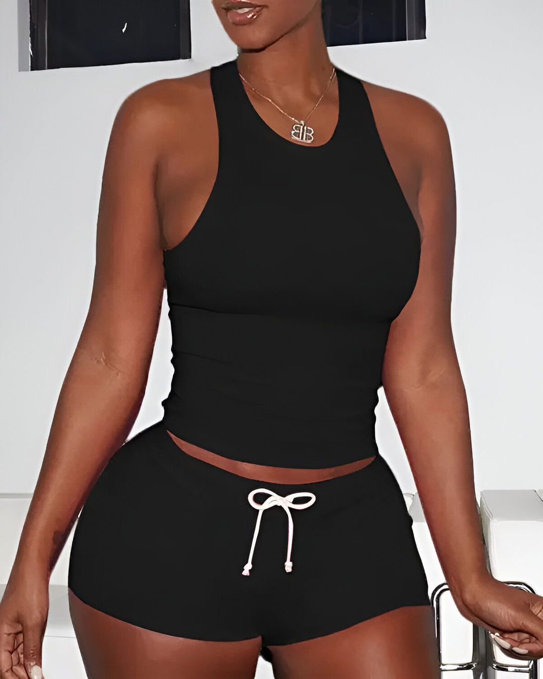 Une femme porte un ensemble de sport noir. Le haut est un débardeur court et le bas est un short taille haute.