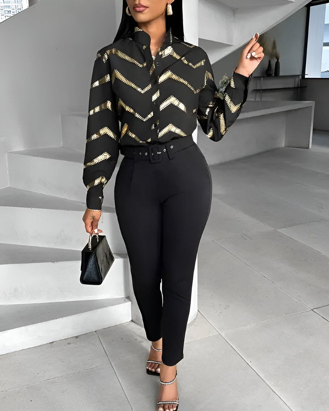 Une femme porte une chemise noire et or avec un pantalon noir. Elle porte également des talons noirs et un sac à main noir.