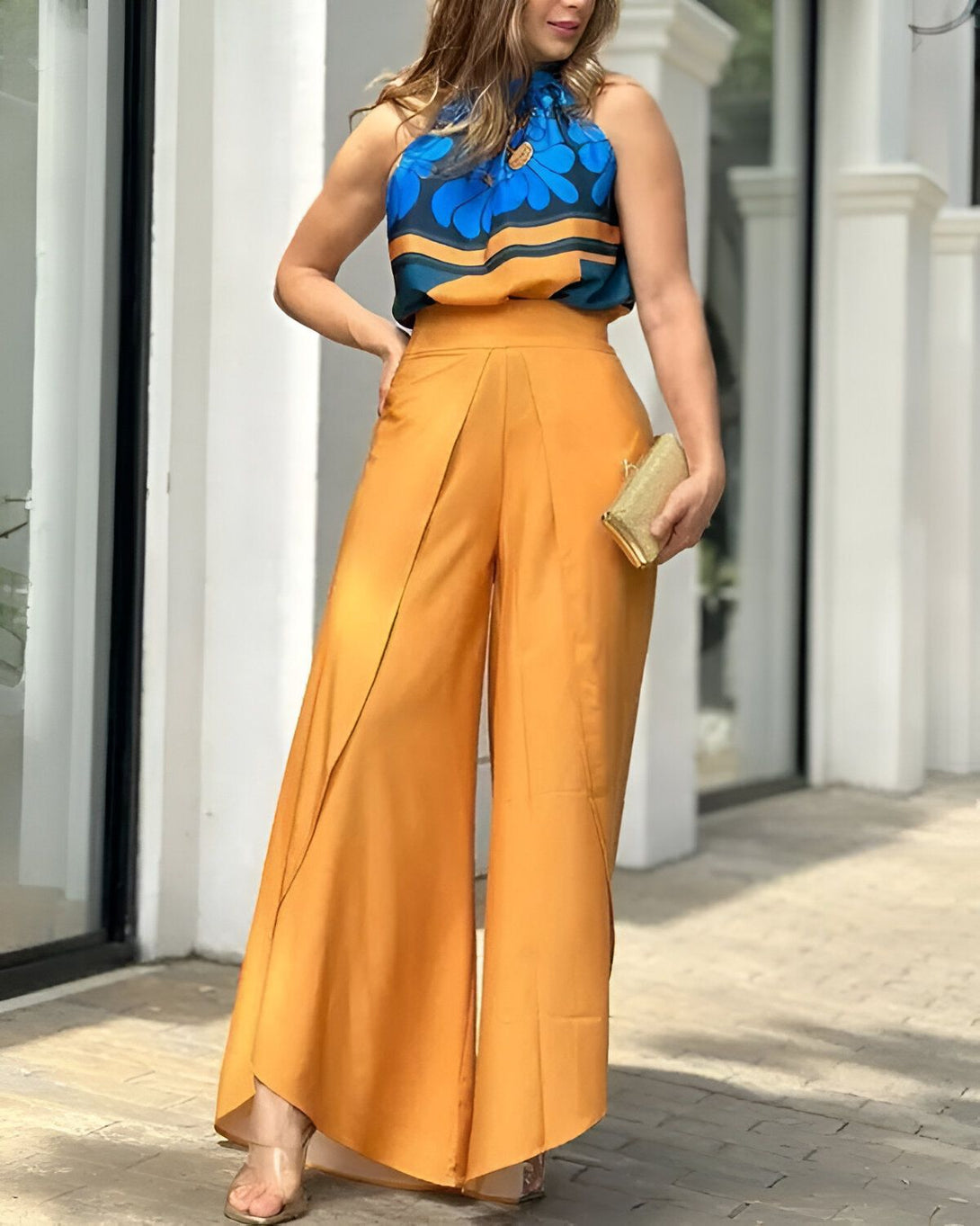 Une femme porte un pantalon large jaune et un haut bleu à motifs. Elle est debout dans la rue et porte des sandales à talons.
