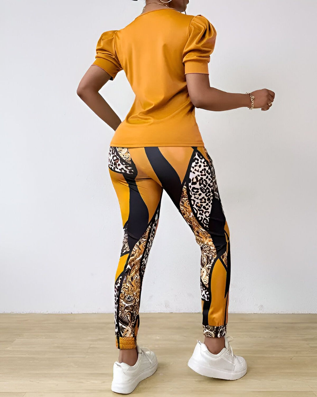 Une femme porte un ensemble pantalon et haut assorti jaune et marron. Le haut a des manches bouffantes et un col rond. Le pantalon est taille haute et a une coupe slim. La femme est vue de dos.