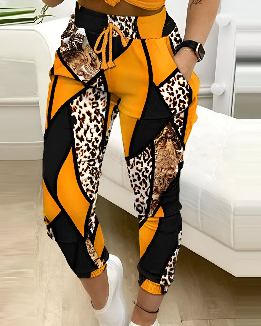Une femme porte un pantalon de jogging jaune, noir et marron. Le pantalon est à motifs léopard et géométriques.