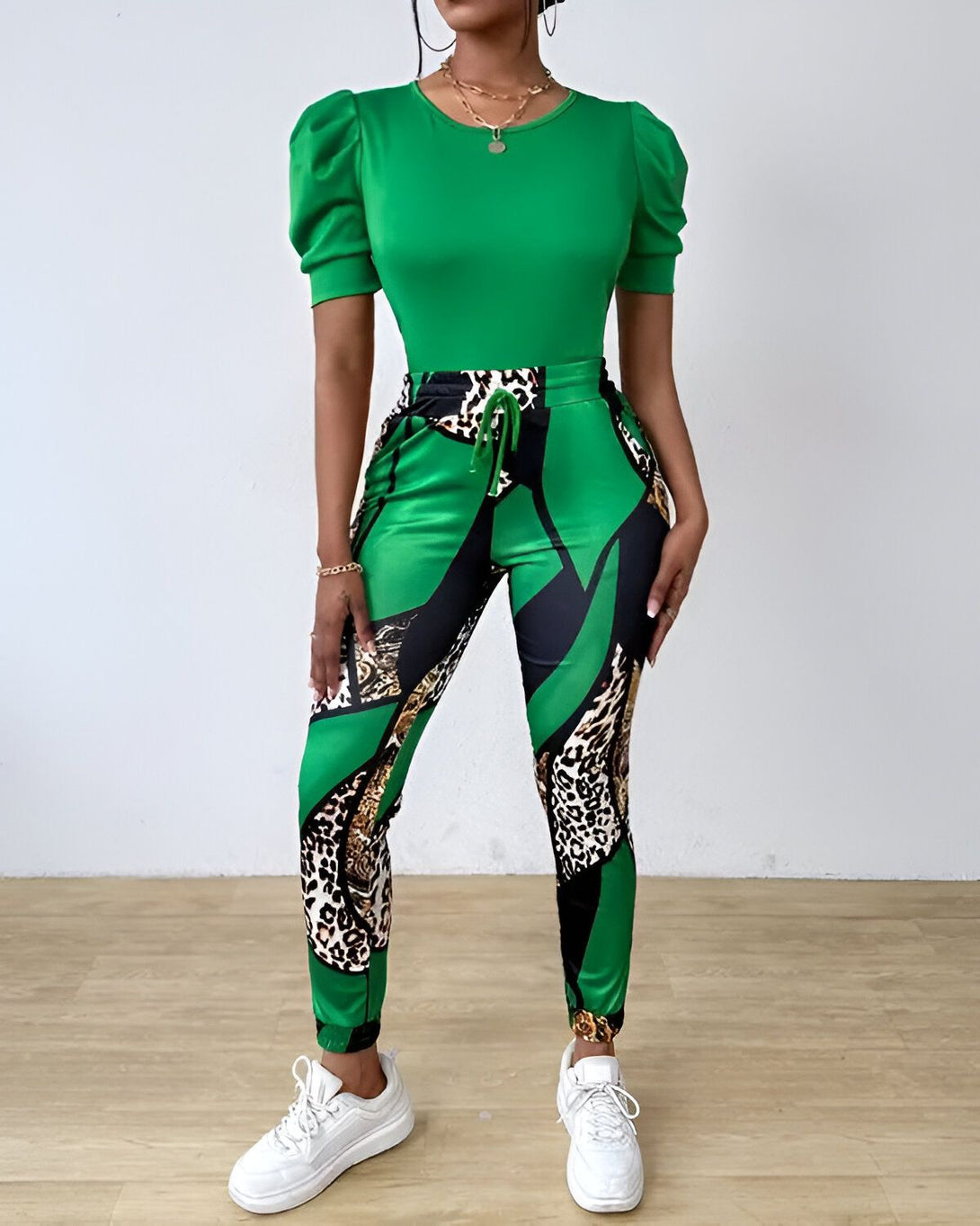 Une femme porte un ensemble vert composé d'un haut à manches bouffantes et d'un pantalon imprimé léopard. Elle porte également des baskets blanches.